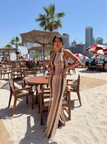 Duga pletena haljina za plažu na pruge zemljanih tonova sa halter dekolteom, vezivanjem na vratu i otvorenim leđima