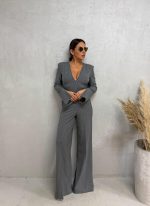 Sivi business kombinezon sa diskretnim belim prugama dugih rasečenih rukava, zvonastih nogavica i V dekoltea